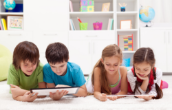 Two boys and two girls laying on the floor and looking at tablets