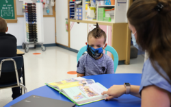 Student at table wearing facemask looking at book with PowerGistics tower in background