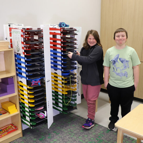 Image shows 2 PowerGistics Core20 charging stations mounted on walls with 2 students next to them.