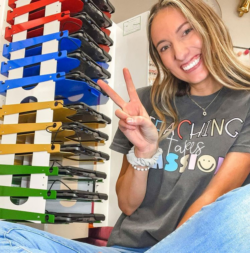 Image shows teacher holding up peace sign sitting next to PowerGistics charging station