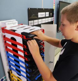 Image shows student retrieving Chromebook from PowerGistics charging station in a classroom