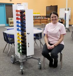 Image shows teacher sitting next to PowerGistics charging station in library